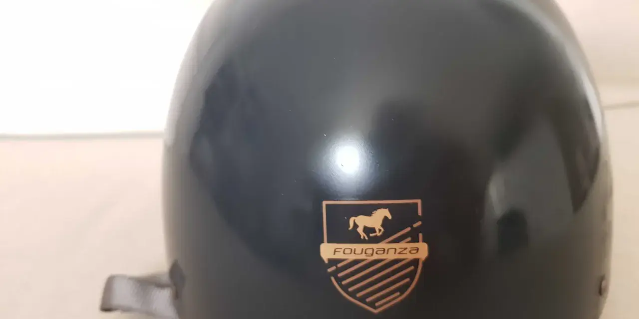Czarny kask jeździecki Fouganza z logo konia i tarczą.