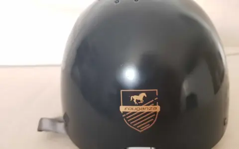 Czarny kask jeździecki Fouganza z logo konia i tarczą.